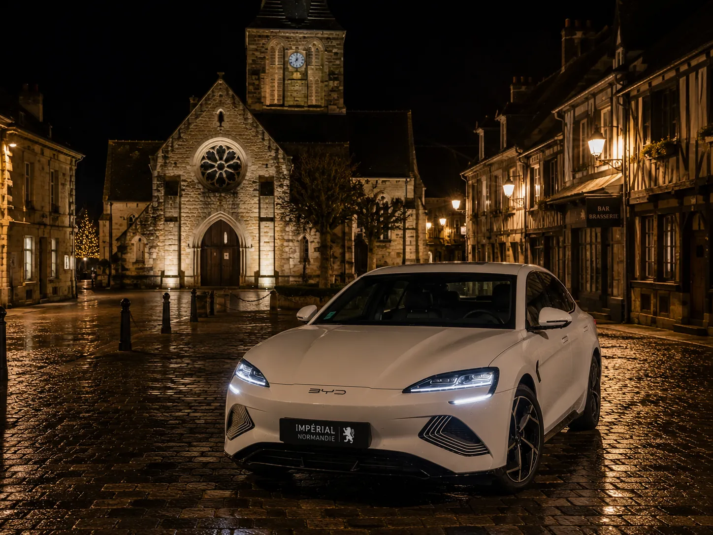 Berline hybride Imperia Normandie de nuit devant une église normande